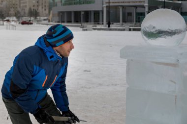 Bir heykeltıraş yontulmuş bir keskiyle buz bloğundan yuvarlak bir buz topu oyuyor..