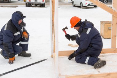 Mavi ceketli bir tesisatçı ahşap bir kirişi ahşap bir kaydırağın çerçevesine ayarlar.