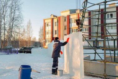 Mavi ceketli bir buzul kasabası müteahhidi, yapım aşamasındaki bir Noel ağacını uzun buz panelleriyle çevreledi.