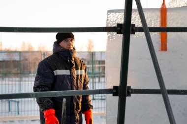 Mavi ceketli bir buzul kasabası müteahhidi, yapım aşamasındaki bir Noel ağacını uzun buz panelleriyle çevreledi.