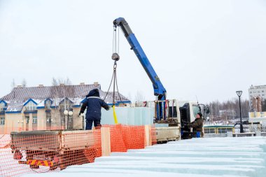 İki montaj işçisi bir arabanın gövdesinden buz kalıplarını boşaltıyor.