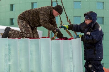 Kışın çalışan işçiler, bir inşaat alanındaki buz bloğunun altına fırlatılan rüzgar kıyafetlerini giyerler.