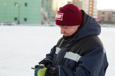 İş tulumlu bir adam telefona bakar.