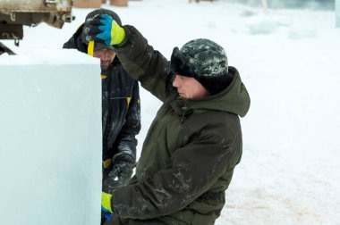 İşçiler buz şehrinin montaj alanındaki buz bloğunu mezurayla işaretliyor