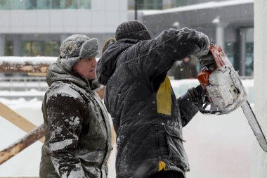 İnşaat alanında çalışan iki işçi, bir benzin testeresiyle buz paneline zarif bir Noel kompozisyonu oyuyorlar..