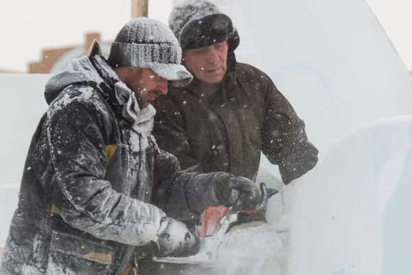 İnşaat alanında çalışan iki işçi, bir benzin testeresiyle buz paneline zarif bir Noel kompozisyonu oyuyorlar..