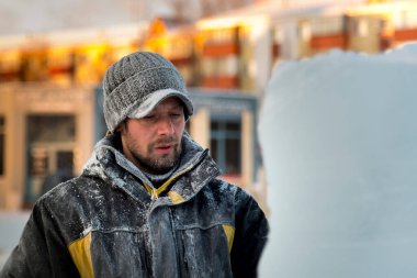 Kışlık ceketli bir montajcının portresi ve buzun yanında güneşliği olan siyah bir şapka.