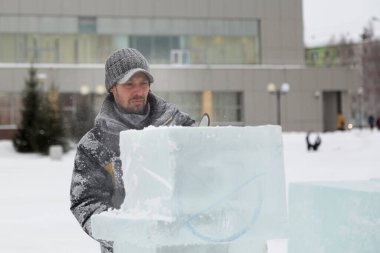 Kışlık ceketli bir montajcının portresi ve buzun yanında güneşliği olan siyah bir şapka.