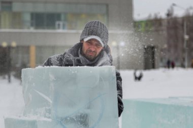 Kışlık ceketli bir montajcının portresi ve buzun yanında güneşliği olan siyah bir şapka.