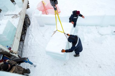 Birleştiriciler vinç kullanarak bir arabadan buz panelleri indirir.