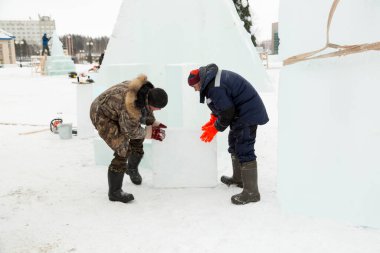 Kış tulumlu işçiler inşaat alanında ellerinde buz kalıbı taşırlar.