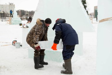 Kış tulumlu işçiler inşaat alanında ellerinde buz kalıbı taşırlar.