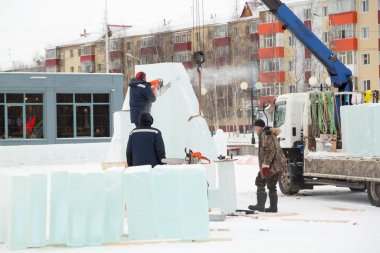Mavi ceketli işçi derleyicisi ve örgülü bir şapka bir buz tabakasını testereyle kesiyor.
