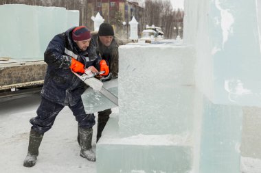 Mavi ceketli işçi derleyicisi ve örgülü bir şapka bir buz tabakasını testereyle kesiyor.