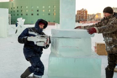 Mavi ceketli işçi derleyicisi ve örgülü bir şapka bir buz tabakasını testereyle kesiyor.