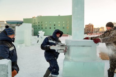 Mavi ceketli işçi derleyicisi ve örgülü bir şapka bir buz tabakasını testereyle kesiyor.