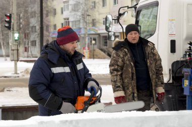 Mavi ceketli işçi derleyicisi ve örgülü bir şapka bir buz tabakasını testereyle kesiyor.
