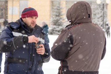 Elinde bir bardak sıcak kahve olan bir işçi, buz kasabasının şantiyesinde çalışan bir meslektaşıyla konuşuyor.