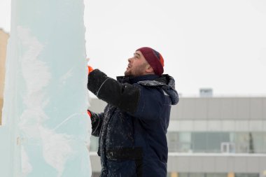 Çalışan bir montajcının portresi mavi ceketli ve buz figürünün yanında örülmüş bir şapka.