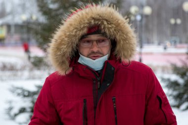 Kırmızı kışlık ceketli, gözlüklü ve yüzünde bandaj olan bir adamın portresi.