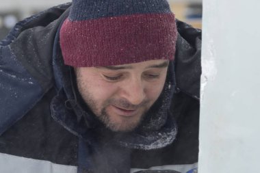 Çalışan bir montajcının portresi mavi ceketli ve buz figürünün yanında örülmüş bir şapka.