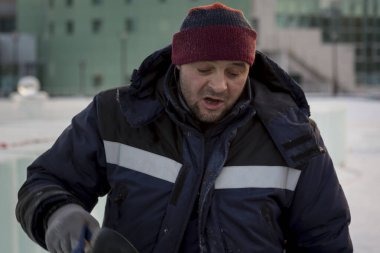 İş yerinde mavi ceketli ve örgü şapkalı bir işçinin yakın çekimi.