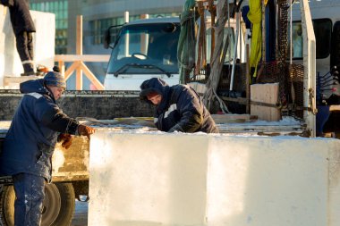 Mavi ceketli ve kafasında kırmızı bir şapka olan işçi bir tesisatçı elektrikli testere ile bir buz plakası kullanıyor.