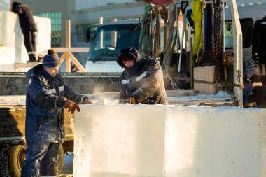 Mavi ceketli ve kafasında kırmızı bir şapka olan işçi bir tesisatçı elektrikli testere ile bir buz plakası kullanıyor.