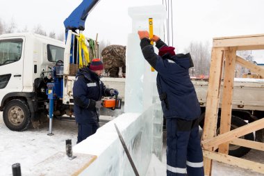 Mavi ceketli ve kafasında kırmızı bir şapka olan işçi bir tesisatçı elektrikli testere ile bir buz plakası kullanıyor.