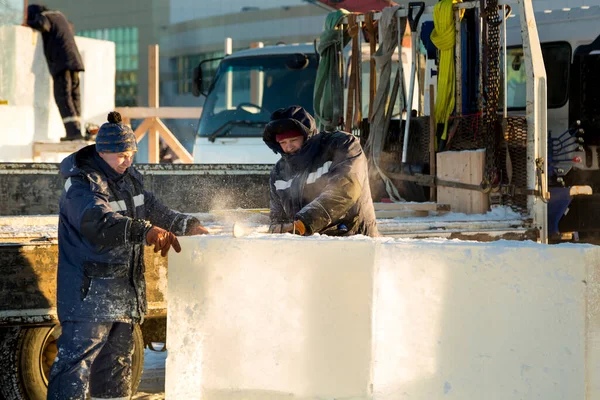 Mavi ceketli ve kafasında kırmızı bir şapka olan işçi bir tesisatçı elektrikli testere ile bir buz plakası kullanıyor.