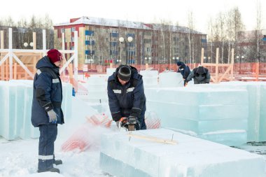 Mavi ceketli bir montaj işçisi ve siyah örülmüş bir şapka bir buz tabakasını testere ile düzeltiyor.