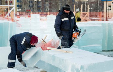 Mavi ceketli ve örgü şapkalı bir işçi buz panelini elleriyle alıyor..