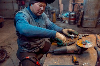 İş yerinde kafasında siyah örgü bir şapkayla kulağında mikrofonla bir kaynakçının portresi.