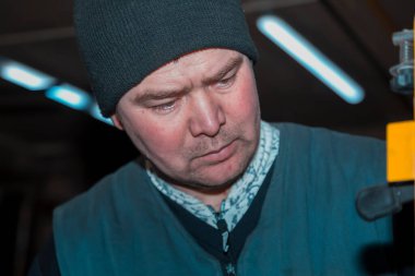 İş yerindeki siyah örgü şapkalı ve kolsuz ceketli bir erkek işçinin yakın plan portresi.