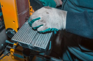 Kemerli zımpara kullanan bir işçi metal bir parçayı işliyor.