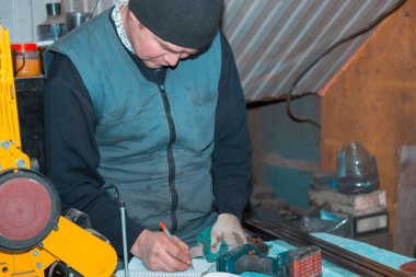 Teypteki usta Emery makinası bir not defterine dolma kalemle bilgi yazıyor.