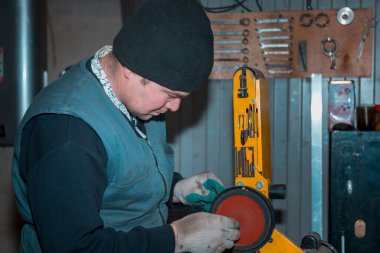Kemerli zımpara kullanan bir işçi metal bir parçayı işliyor.