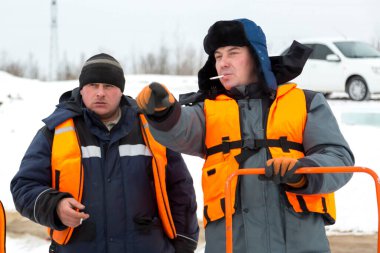 Turuncu can yelekli işçiler donmuş bir gölün buzunda sigara molası verdiler.