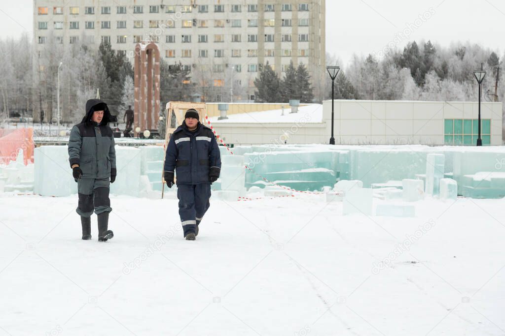 Two assemblers walk along the construction site of the ice town