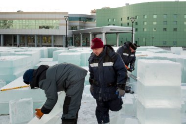 Bir işçi buz kasabası boyunca kollarında bir buz bloğu taşıyor.