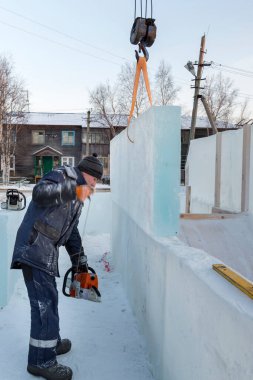 Mavi ceketli ve örgü şapkalı çalışan bir derleyici elektrikli testere ile buz kalıbı sürüyor.