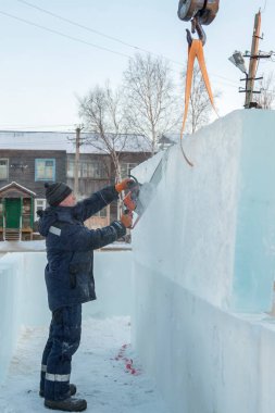 Mavi ceketli ve örgü şapkalı çalışan bir derleyici elektrikli testere ile buz kalıbı sürüyor.