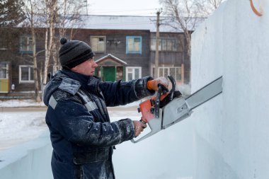 Mavi ceketli ve örgü şapkalı çalışan bir derleyici elektrikli testere ile buz kalıbı sürüyor.