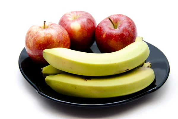 Красные яблоки с бананами на черной тарелке — стоковое фото