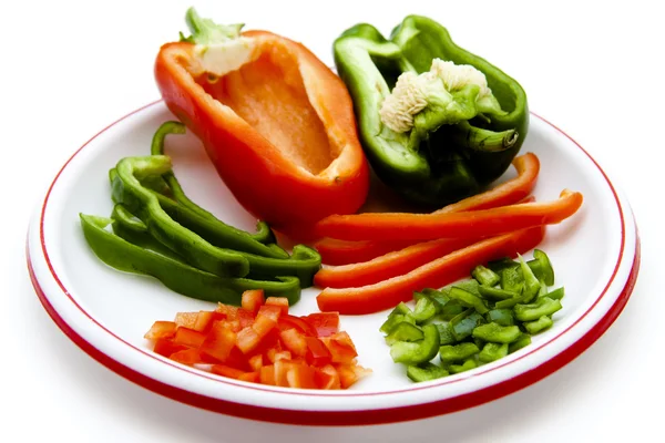 Red and green paprika in pieces and stripes on plate Royalty Free Stock Photos