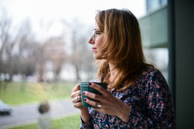 Kahve içen ve pencereden dışarı bakan kadın.