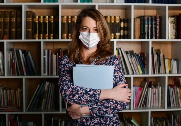 Young woman with mask for corona virus holding big books in library. Business girl at the office