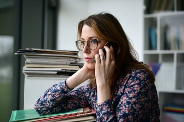 Pretty woman talking on phone near window in room. Serious female having phone talk