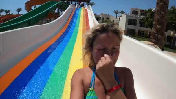 若い女性は大きな多色のウォータースライドを滑り降りてプールに飛び込みます。4kビデオ — ストック動画