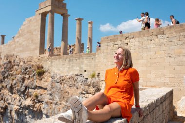 Yunanistan 'ın Akropolis kentindeki Partenon' un arka planında, harabeler içinde oturmuş gülümseyen siyah Hipster yolcusu. Tatildeki kadın Atina ziyaretinin keyfini çıkarıyor
